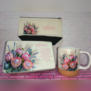 Floral-themed desk set: a metal tin, a notebook, and a mug, all with bright pink protea-style flowers and lavender on a pink brick background.