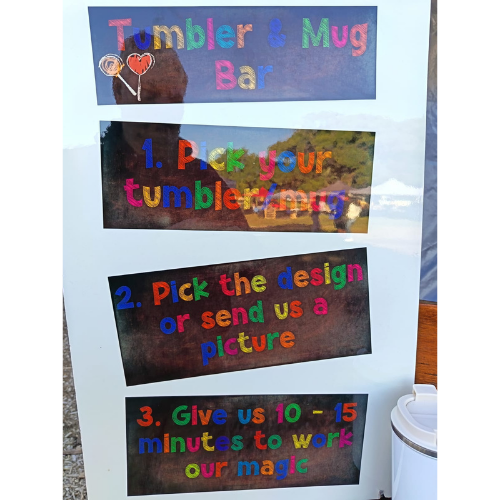 Sign labeled 'Tumbler & Mug Bar' showing three steps: 1) Pick your tumbler/mug, 2) Pick the design or send us a picture, 3) Give us 10–15 minutes to work our magic.